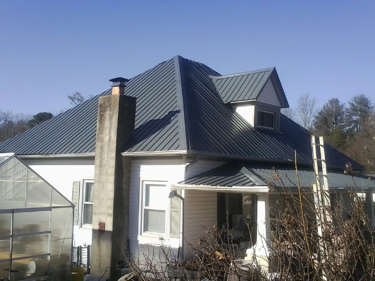 Dark blue standing seam metal roof on a white farmhouse with dormer — Slate & Tile Roof Repair by Roofing Brothers in Urbanna
