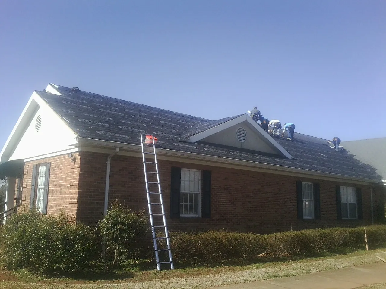 Crew tearing shingles off a brick ranch roof with a ladder set — Emergency Roof Repair work by our crew in Urbanna