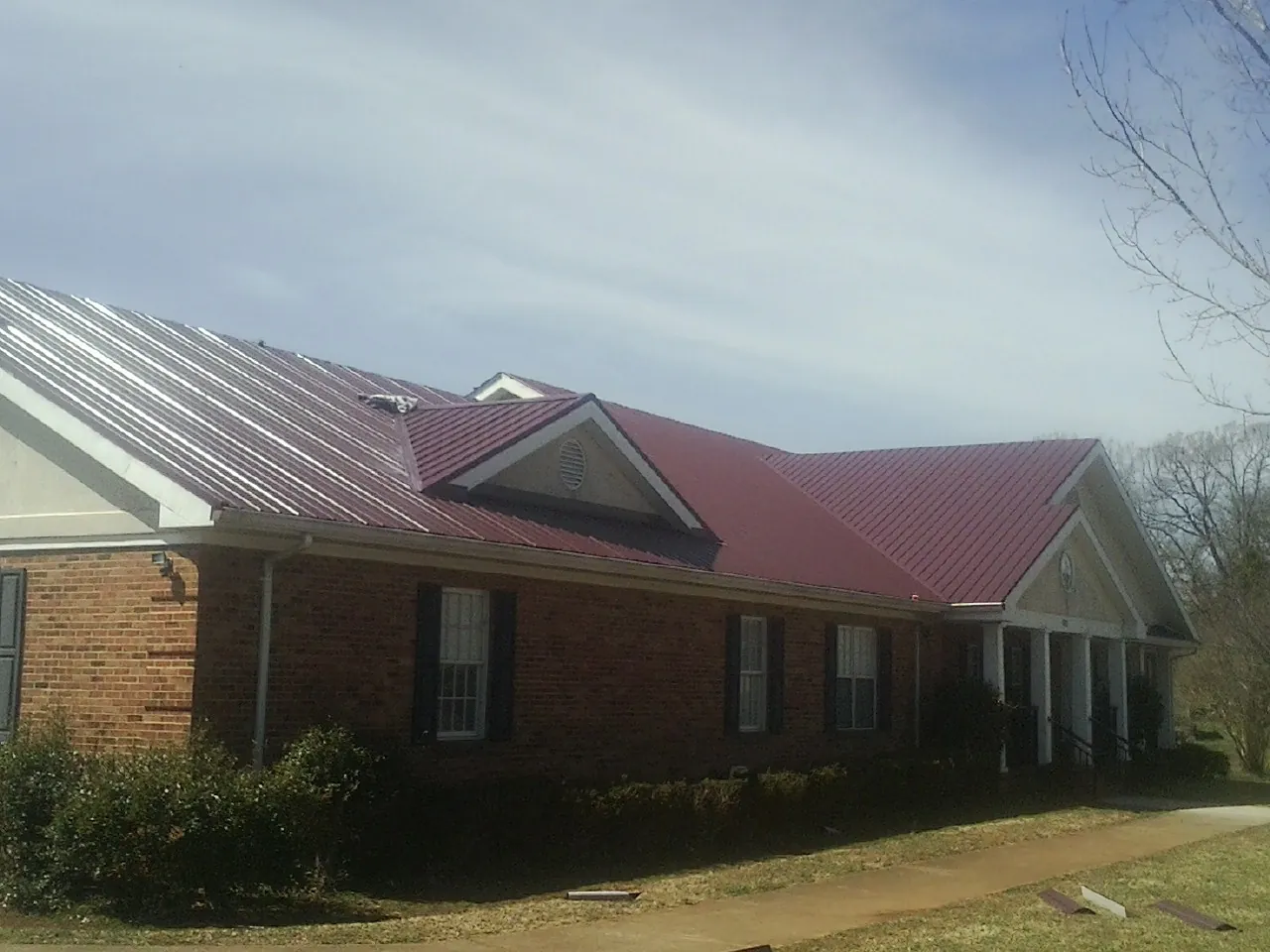 Red metal roof with gabled entries on a long brick building, from a Hail Damage Roof Repair job in Urbanna
