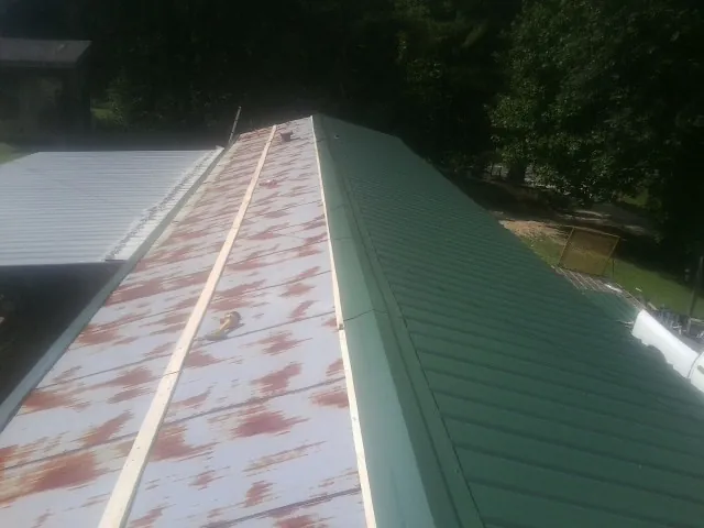 Old rusted panels beside newly installed green metal roofing — Wind Damage Roof Repair by Roofing Brothers in Urbanna