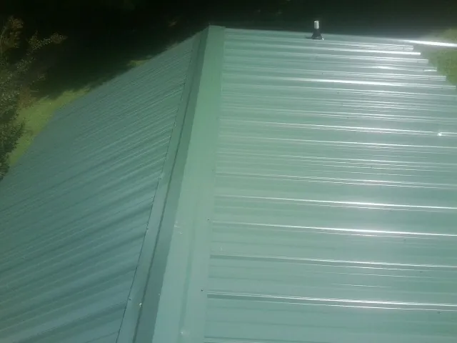 New green metal panels meeting at the ridge of a roof — Flat Roof Repair work by our crew in Urbanna