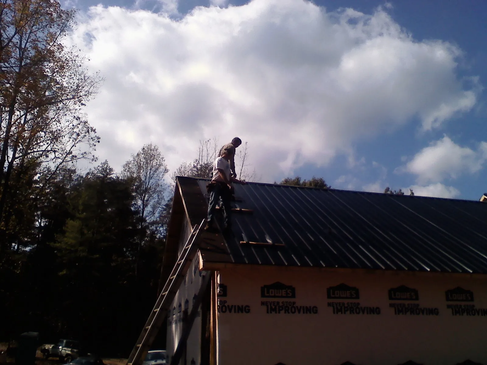 Roofer fastening dark metal panels high against a cloudy sky, from a Roof Inspection job in Urbanna