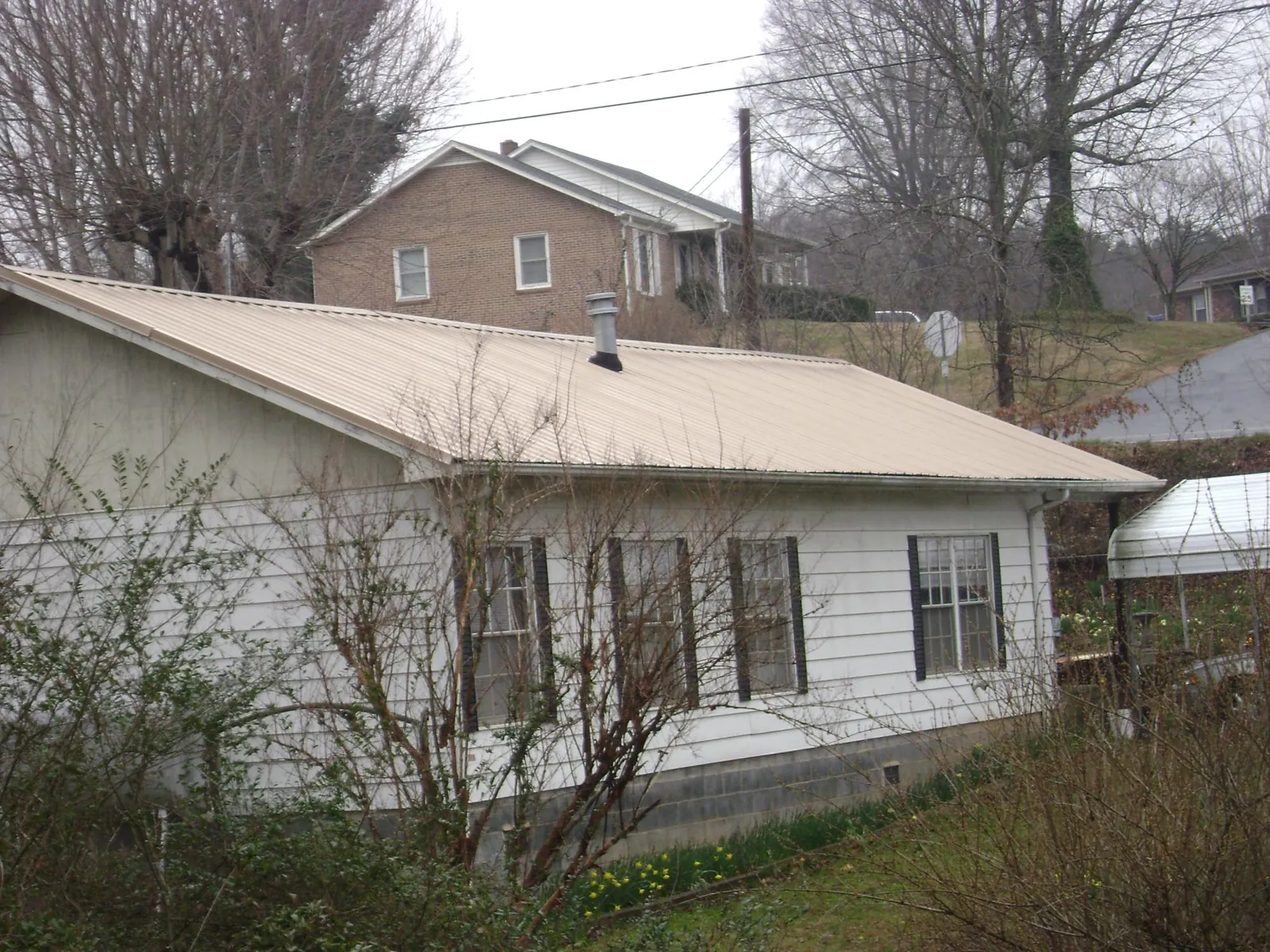 Tan metal roof on a white sided house set into a hillside — Commercial Roofing by Roofing Brothers in Urbanna